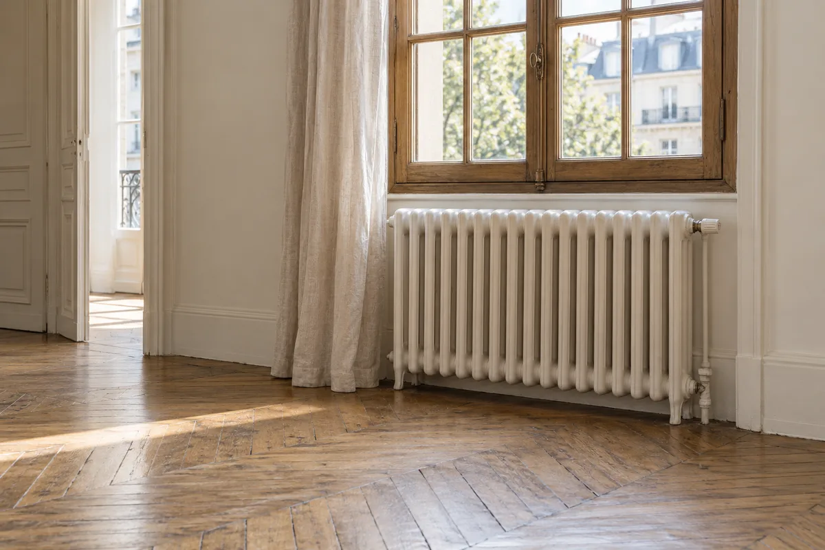 Radiateur ancien en fonte sous une fenêtre à petits carreaux dans un salon vide
